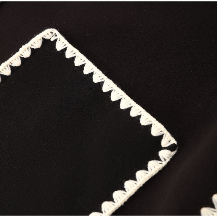 Schwarzer Stoff mit weißem Zickzack-Stichmuster an den Rändern. Hochwertiges Textildesign, ideal für Mode und Inneneinrichtung.
