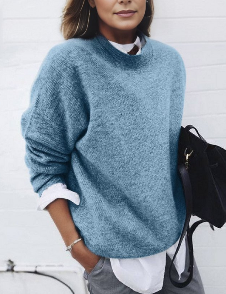 Frau in blauem Strickpullover und weißem Hemd, hält schwarze Tasche. Modetrend Herbst, lässiger Stil, elegante Damenmode.