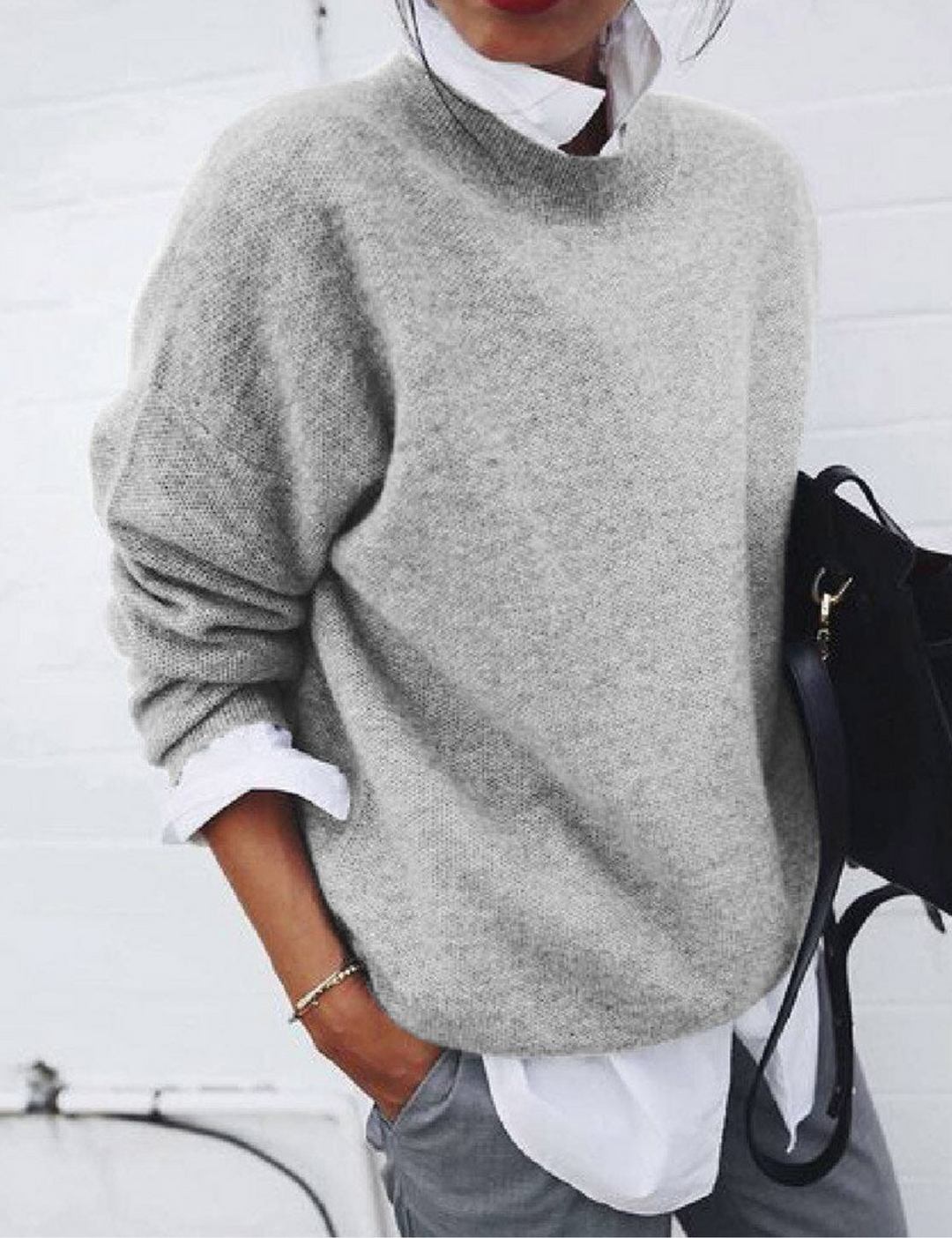 Frau in grauem Pullover und weißem Hemd, hält schwarze Tasche. Modischer Herbst-Look, lässiger Stil, Damenmode, Streetwear-Trend.