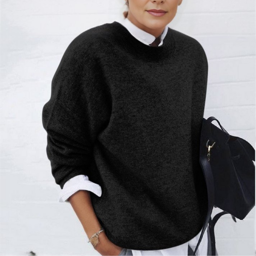 Frau in schwarzem Pullover und weißem Hemd vor weißer Wand, hält schwarze Tasche. Modetrend, Herbstmode, eleganter Look.