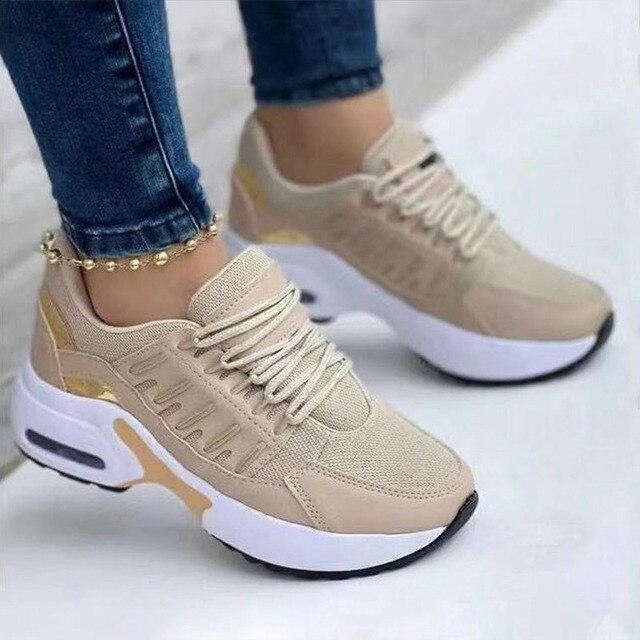 Beige Damen-Sneaker mit weißer Sohle, goldenen Akzenten und Schnürsenkeln, getragen von Person in blauen Jeans. Modische Sportschuhe.