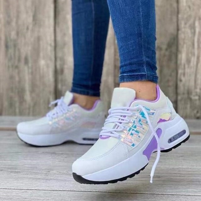 Damen-Sneaker mit weißem Obermaterial, lila Akzenten und Luftpolstersohle, getragen mit blauen Jeans vor Holzhintergrund. Trendige Sportschuhe.
