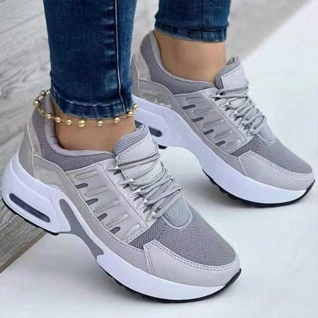 Graue Damen-Sneaker mit weißer Sohle, getragen mit blauer Jeans und goldener Fußkette. Modische Sportschuhe, bequem und stilvoll.