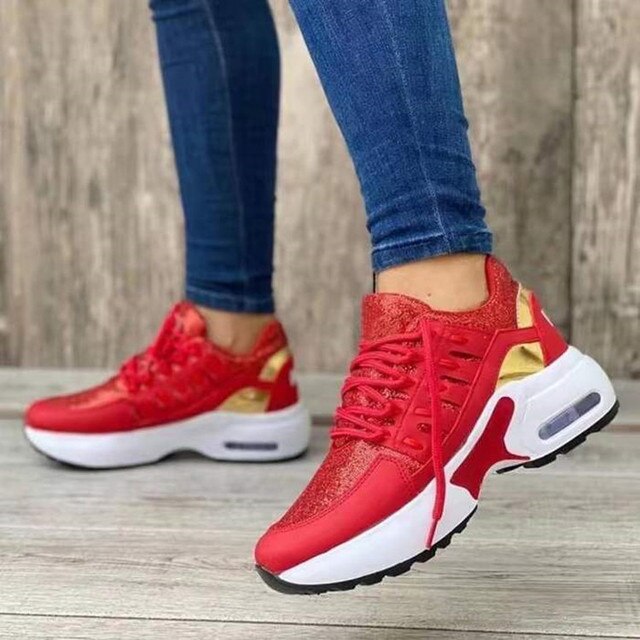 Rote Damen-Sneaker mit goldenen Akzenten, weißer Sohle und schwarzem Profil. Getragen mit blauen Jeans vor einem Holzhintergrund.