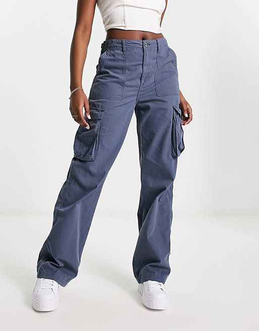 Frau in blauer Cargohose und weißem Top, modische Streetwear, lässiger Stil, trendige Damenmode, bequeme Passform, weiße Sneaker.