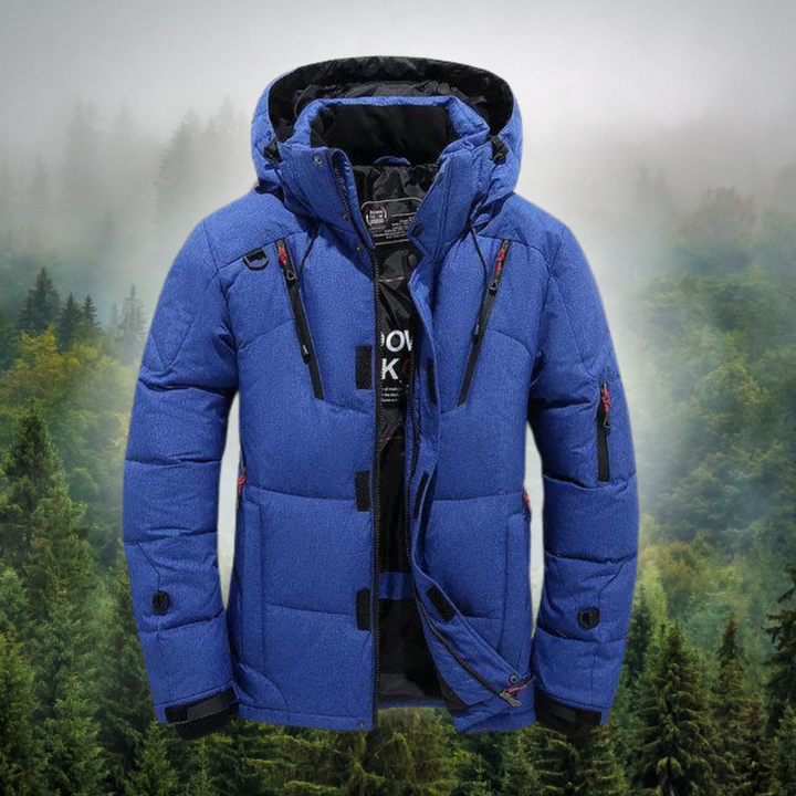 Blaue Winterjacke mit Kapuze vor nebligem Waldhintergrund, Outdoor-Bekleidung, warme Daunenjacke, wetterfest, ideal für kalte Temperaturen.