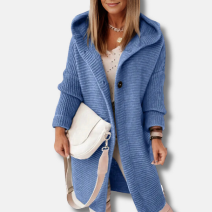 Frau in blauem Strickmantel mit Kapuze, weißem Oberteil und weißer Umhängetasche. Modetrend Herbst, Damenmode, stilvoller Look.