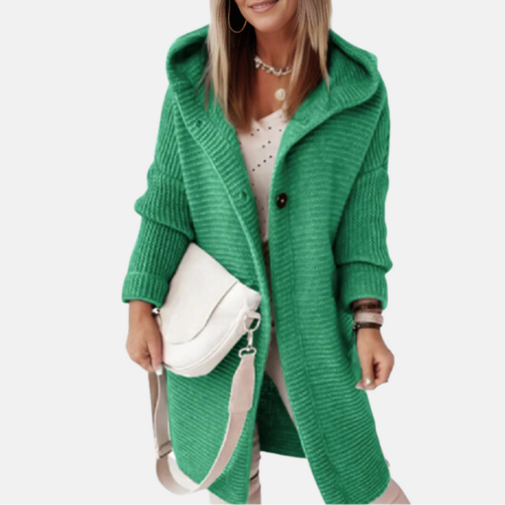 Frau in grünem Strickmantel mit Kapuze, weißem Top und Umhängetasche. Modetrend Herbst, Damenmode, stilvoller Look.