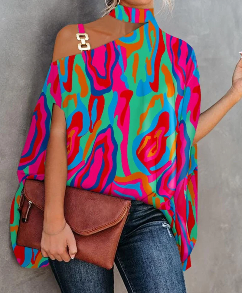 Frau in bunter, schulterfreier Bluse mit abstraktem Muster, hält braune Clutch. Modetrend, auffällige Kleidung, Streetstyle.