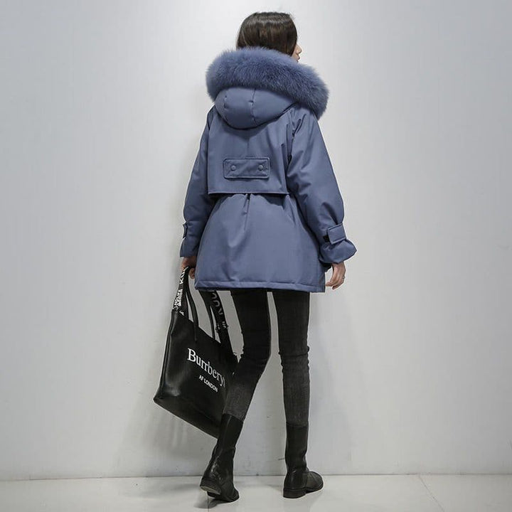 Frau in blauer Winterjacke mit Fellkapuze, schwarze Jeans und Stiefel, trägt schwarze Burberry-Tasche. Elegante Wintermode, stilvoller Look.