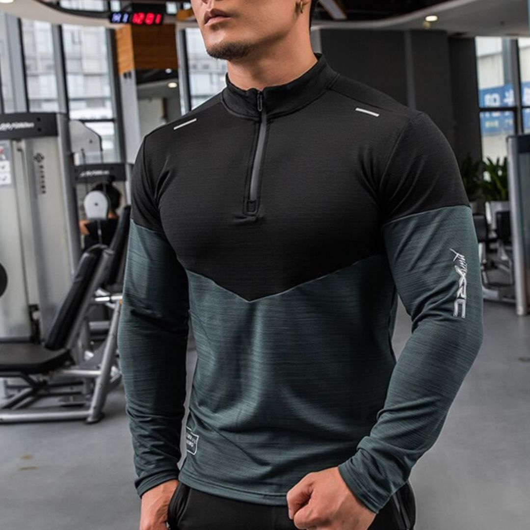 Mann im Fitnessstudio trägt schwarzes und graues Kompressionsshirt, muskulös, sportlich, Fitnessmode, Langarm, Reißverschluss, moderne Sportbekleidung.