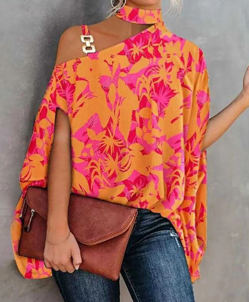 Frau in bunter, schulterfreier Bluse mit tropischem Muster, hält braune Lederhandtasche. Modetrend, Sommeroutfit, Damenmode.