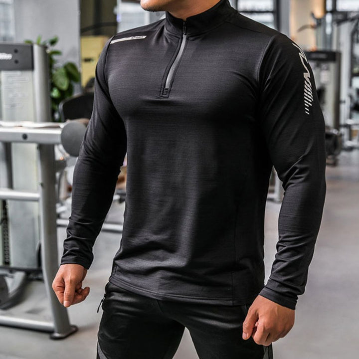 Mann im schwarzen Sport-Oberteil im Fitnessstudio, muskulös, Langarm, Reißverschluss, moderne Fitnesskleidung, Krafttraining, Sportmode.