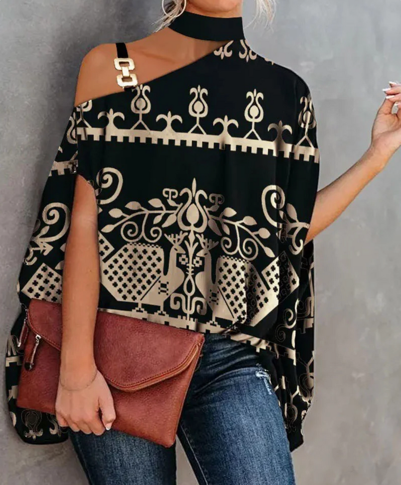 Frau in modischer schwarzer Tunika mit goldenen Mustern, asymmetrischem Schnitt und Schulterriemen, hält braune Clutch, trägt Jeans.