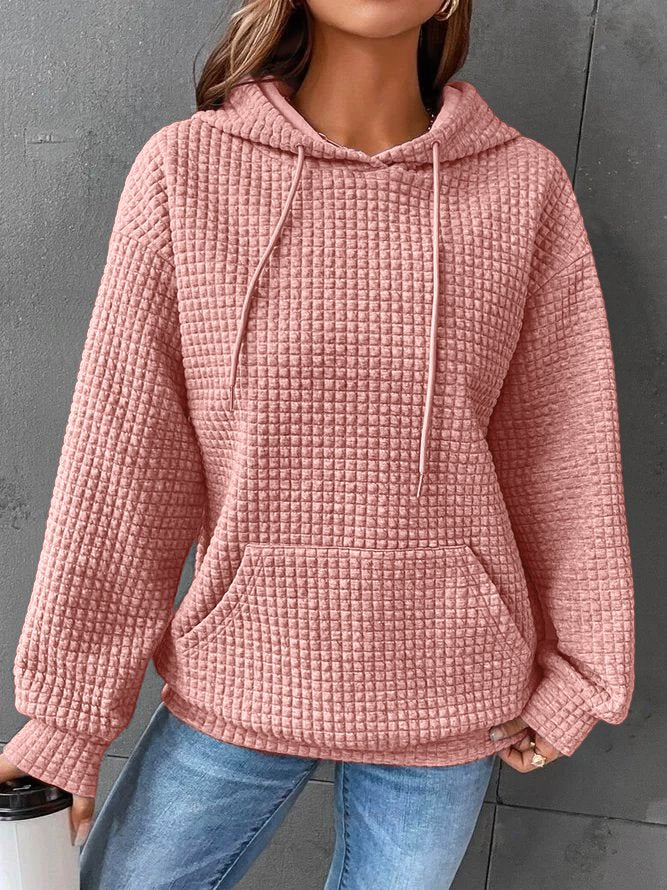 Frau in rosa Kapuzenpullover mit Waffelmuster, lässig und modisch, hält einen weißen Becher. Perfekt für Herbstmode und Freizeitkleidung.