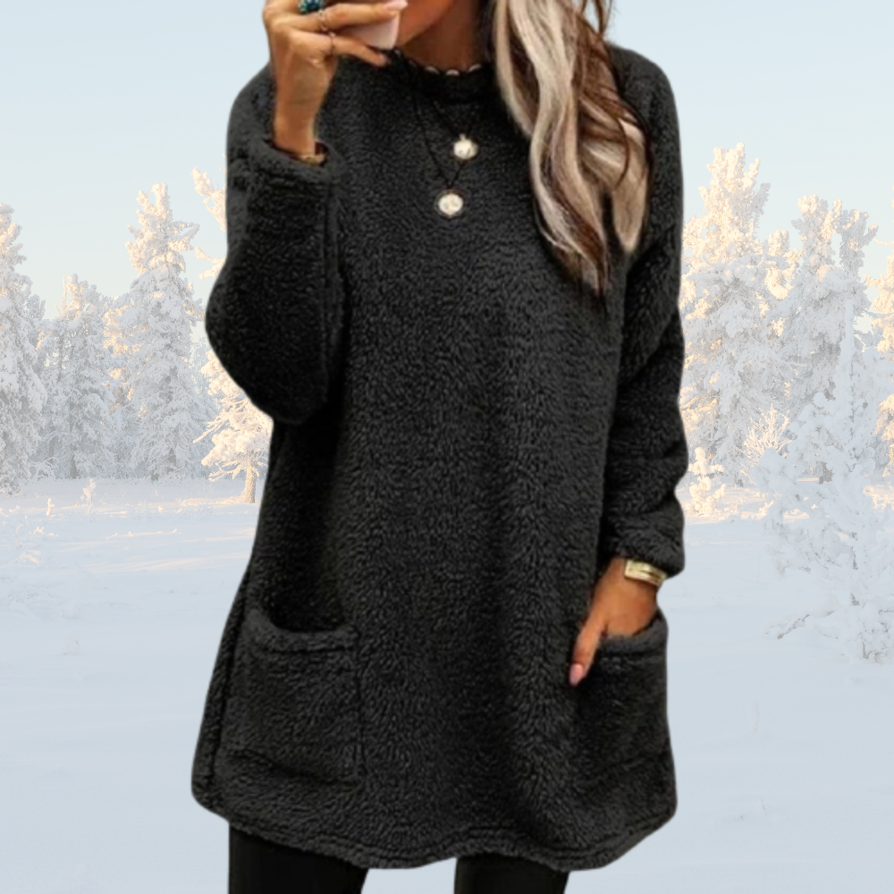 Frau in schwarzem Fleece-Pullover mit Taschen, winterliche Schneelandschaft im Hintergrund. Modischer Winterlook, gemütlicher Pullover, Damenmode.