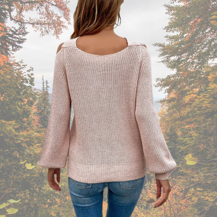 Rückansicht einer Frau in einem rosa Strickpullover und blauen Jeans, umgeben von herbstlicher Waldlandschaft. Perfekt für Herbstmode-Inspiration.