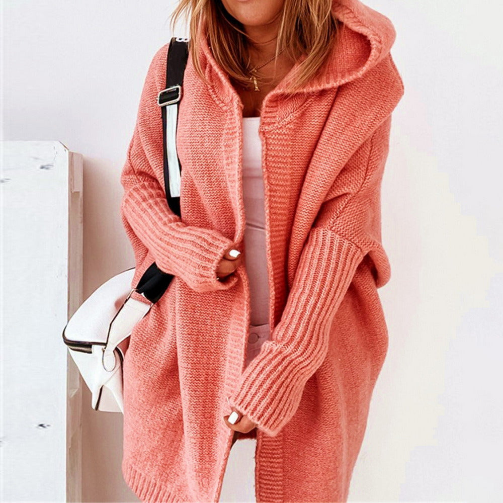 Frau in rosa Strick-Cardigan mit Kapuze, weißem Top und weißer Umhängetasche. Modetrend, gemütlicher Herbst-Look, Damenmode.