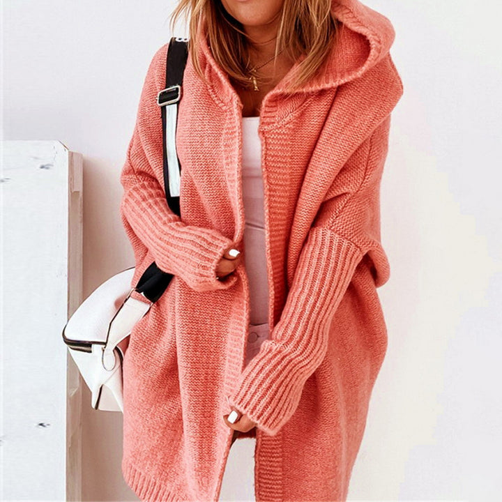 Frau in rosa Strick-Cardigan mit Kapuze, weißem Top und weißer Umhängetasche. Modetrend, gemütlicher Herbst-Look, Damenmode.