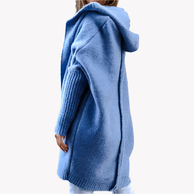 Frau in blauem Strickmantel mit Kapuze, steht vor einem weißen Hintergrund. Modetrend, Wintermode, gemütlicher Look, urbaner Stil.
