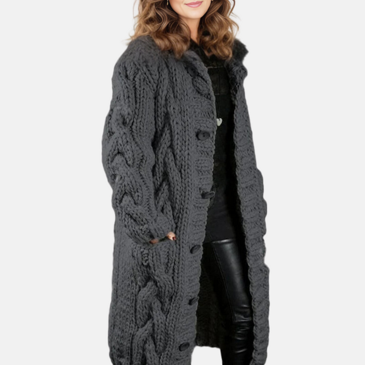Dame in langem, grauem Strickmantel mit Zopfmuster, schwarze Lederhose. Modetrend, Wintermode, Damenbekleidung, stilvoller Look.