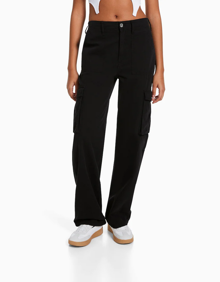 Frau trägt schwarze Cargo-Hose mit Taschen, kombiniert mit weißen Sneakers. Modetrend, lässiger Stil, Damenbekleidung, Streetwear.