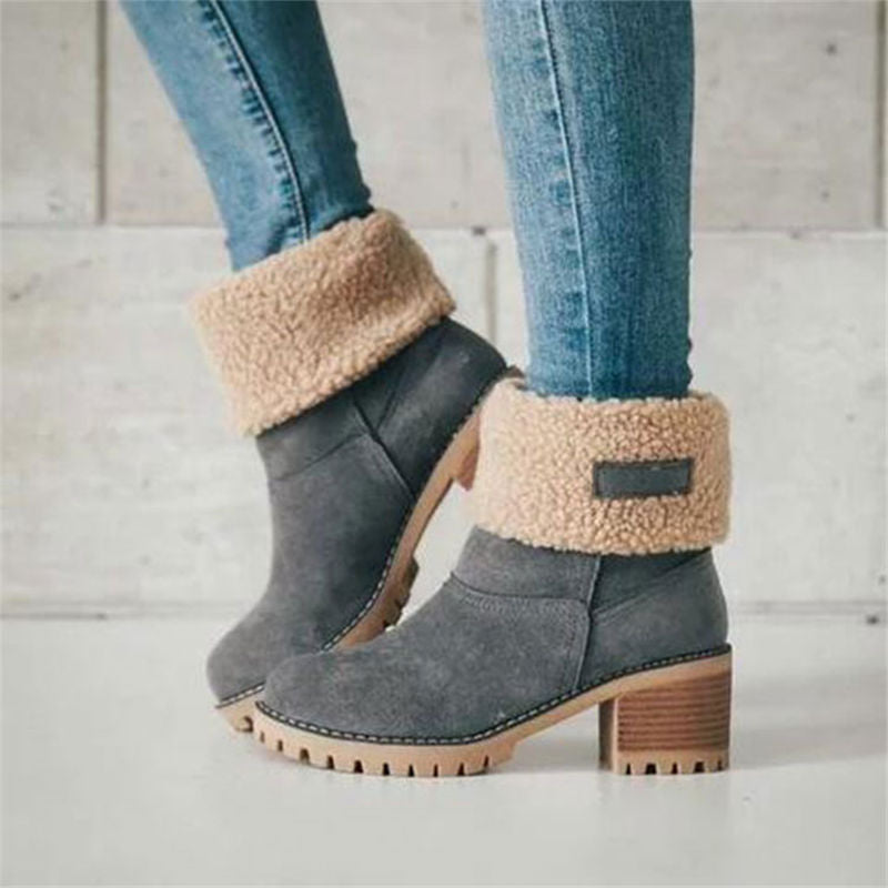 Graue Damenstiefel mit Absatz, gefüttert mit beigem Kunstfell, kombiniert mit blauen Jeans. Modische Winterstiefel, ideal für kaltes Wetter.