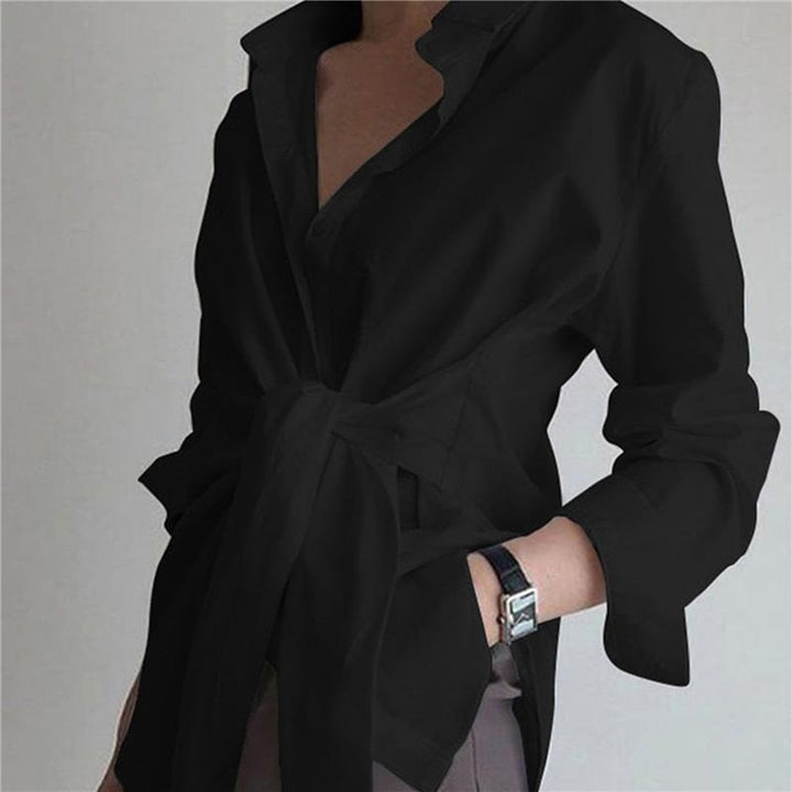Frau in schwarzer Bluse mit Gürtel, Hand in Hosentasche, elegantes Outfit, minimalistischer Stil, modisches Accessoire, Armbanduhr.