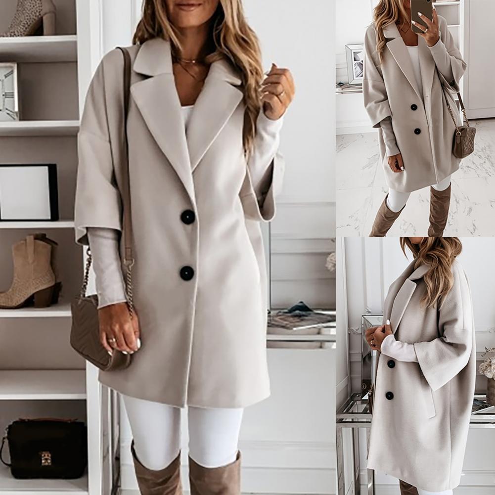 Frau in beigem Mantel, weißem Oberteil und Hose, braune Stiefel, posiert vor Regal. Modetrend, Herbstmode, eleganter Look, Damenbekleidung.