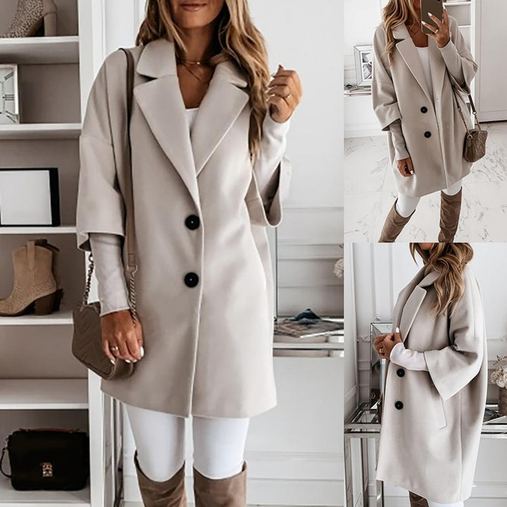 Frau in beigem Mantel, weißem Oberteil und Hose, braune Stiefel, posiert vor Regal. Modetrend, Herbstmode, eleganter Look, Damenbekleidung.