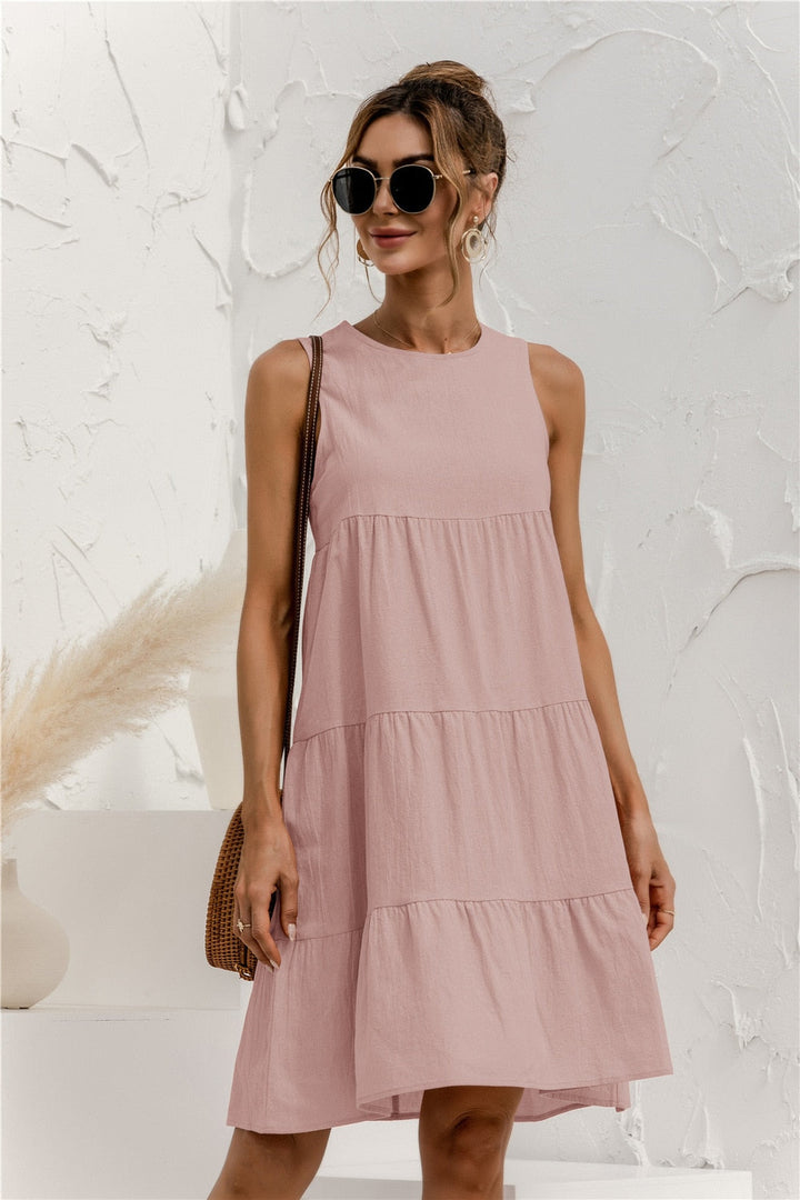 Frau in rosa Sommerkleid mit Sonnenbrille, brauner Tasche, vor weißer Wand. Modetrend, Damenmode, Sommeroutfit, lässiger Stil.