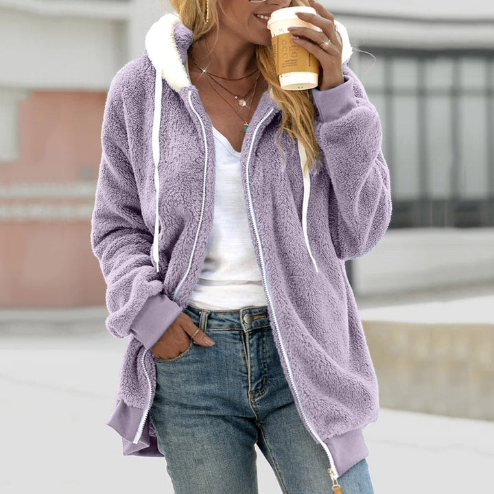 Frau in lila Teddy-Fleecejacke mit Kapuze, hält Kaffeebecher. Modetrend Herbst, lässiger Streetstyle, gemütliche Damenbekleidung.