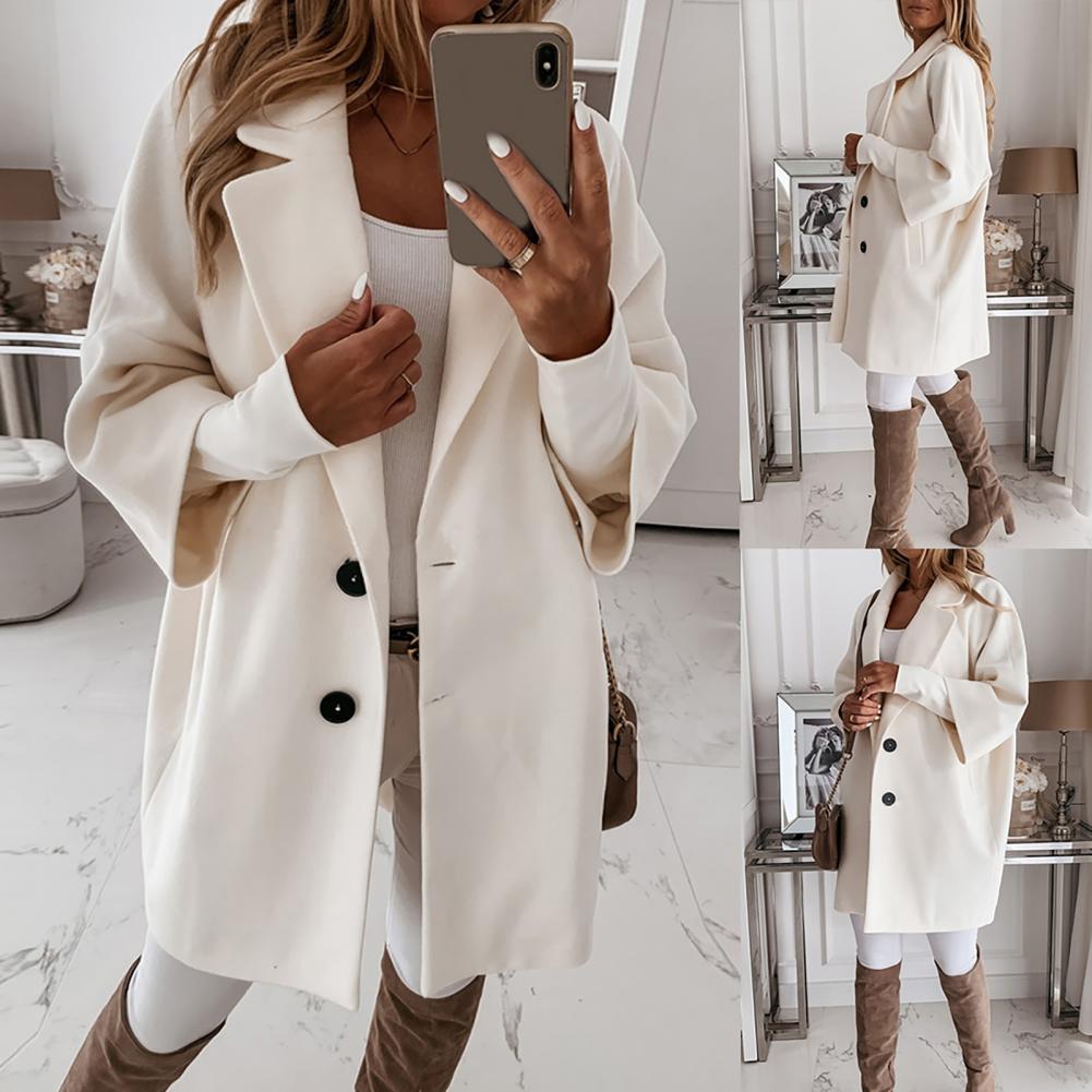 Frau in elegantem weißen Mantel, kombiniert mit braunen Stiefeln und weißem Outfit, posiert in modernem, stilvollem Interieur. Fashion, Herbstmode.