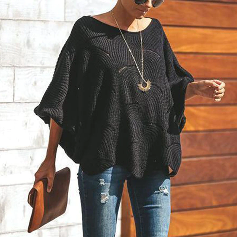 Frau in schwarzem Oversize-Pullover, zerrissene Jeans, braune Clutch, Sonnenbrille, Holz- und Steinwand im Hintergrund. Modetrend, lässiger Stil.