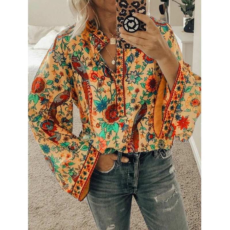 Frau in bunter, geblümter Bluse mit langen Ärmeln, hält Smartphone mit gemustertem Case, trägt zerrissene Jeans. Modetrend, Boho-Stil, Damenmode.