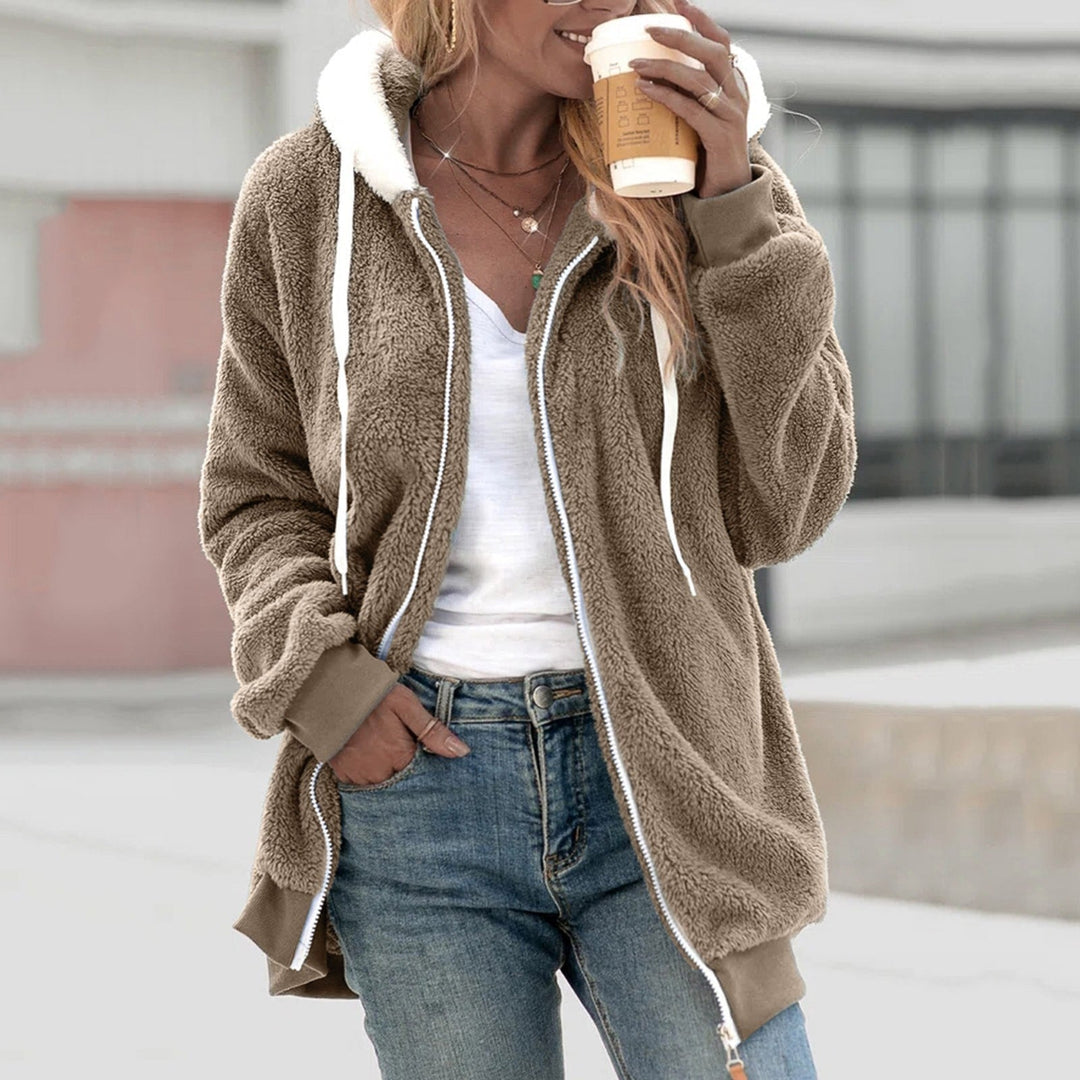 Frau in brauner Teddyjacke mit Kapuze, hält Kaffeebecher, trägt weiße Bluse und Jeans. Herbstmode, lässiger Stil, Outdoor-Kleidung.