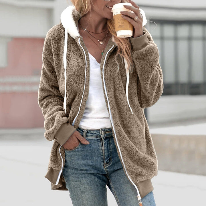 Frau in brauner Teddyjacke mit Kapuze, hält Kaffeebecher, trägt weiße Bluse und Jeans. Herbstmode, lässiger Stil, Outdoor-Kleidung.