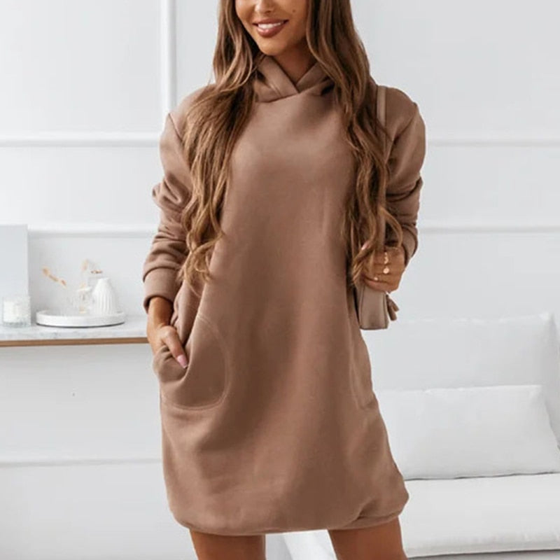 Frau in braunem Hoodie-Kleid mit langen Ärmeln, lässiger Stil, moderne Mode, gemütliches Wohnzimmer, trendige Damenbekleidung.