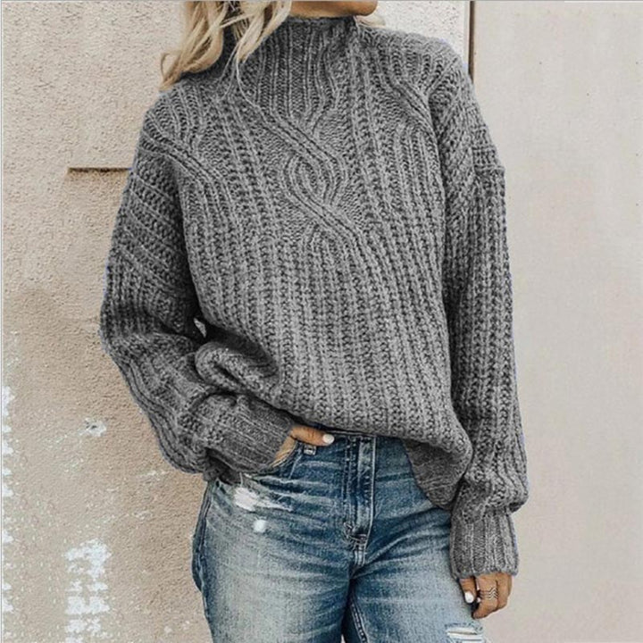 Grauer Strickpullover mit Zopfmuster, getragen von einer Person in blauen Jeans. Modischer Winterlook, gemütlicher Pullover, lässiger Stil.