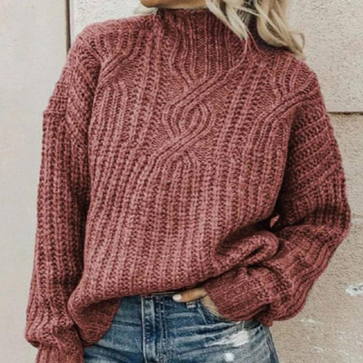 Roter Strickpullover mit Zopfmuster, hochgeschlossen, kombiniert mit blauen Jeans. Modischer Damen-Winterlook, gemütlich und stilvoll.