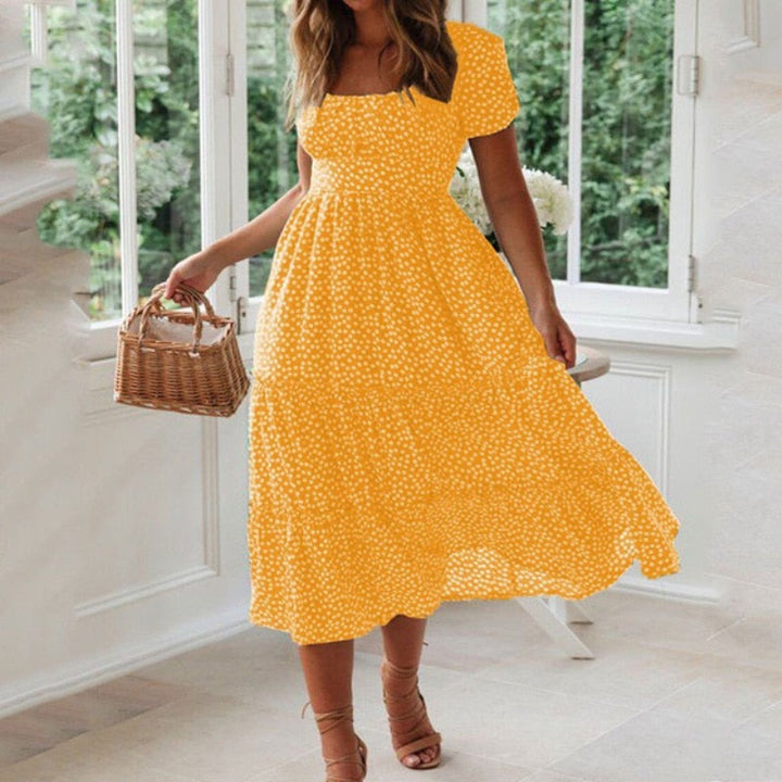 Frau in gelbem Sommerkleid mit weißen Punkten, hält einen Korb in der Hand, steht in einem hellen Raum mit großen Fenstern. Sommermode, Damenkleid.