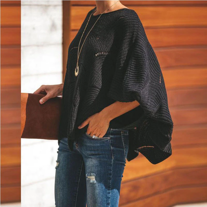 Schwarzer Strickponcho, lässig über Jeans getragen, mit brauner Clutch. Modetrend Herbst, Damenmode, eleganter Freizeitlook, urbaner Stil.
