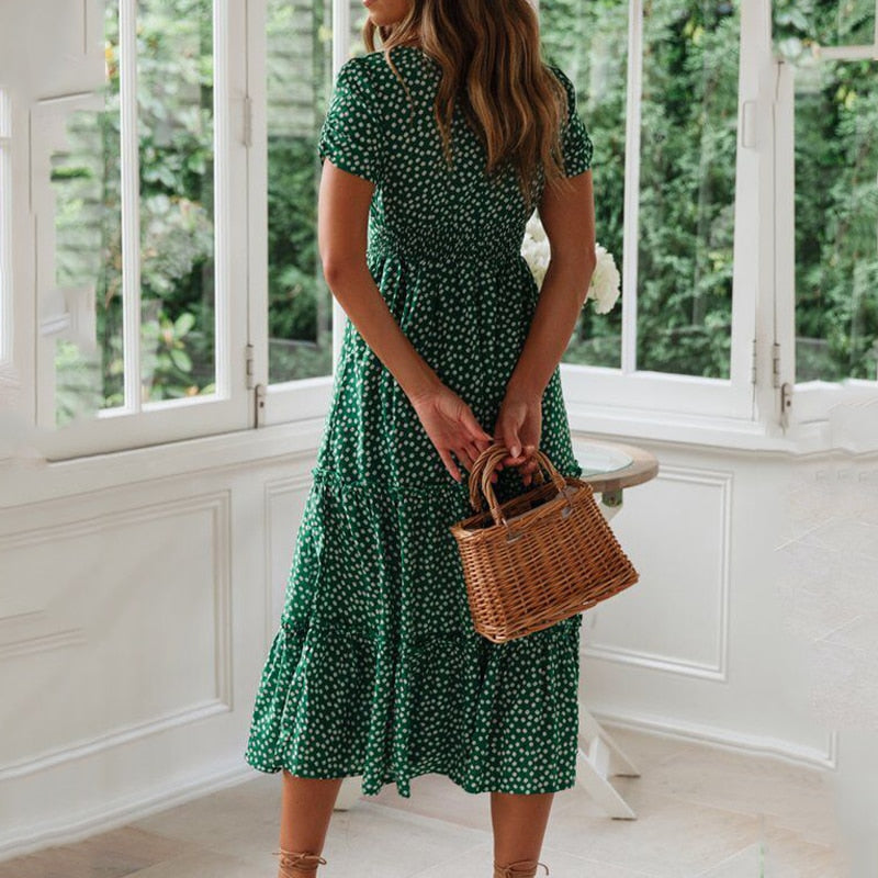 Frau in grünem, gepunktetem Kleid mit Korbtasche steht in hellem Raum vor großen Fenstern. Sommermode, Damenkleid, Korbtasche, Innenraum.