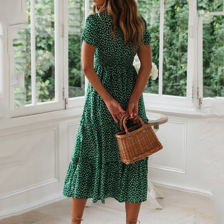 Frau in grünem, gepunktetem Kleid mit Korbtasche steht in hellem Raum vor großen Fenstern. Sommermode, Damenkleid, Korbtasche, Innenraum.
