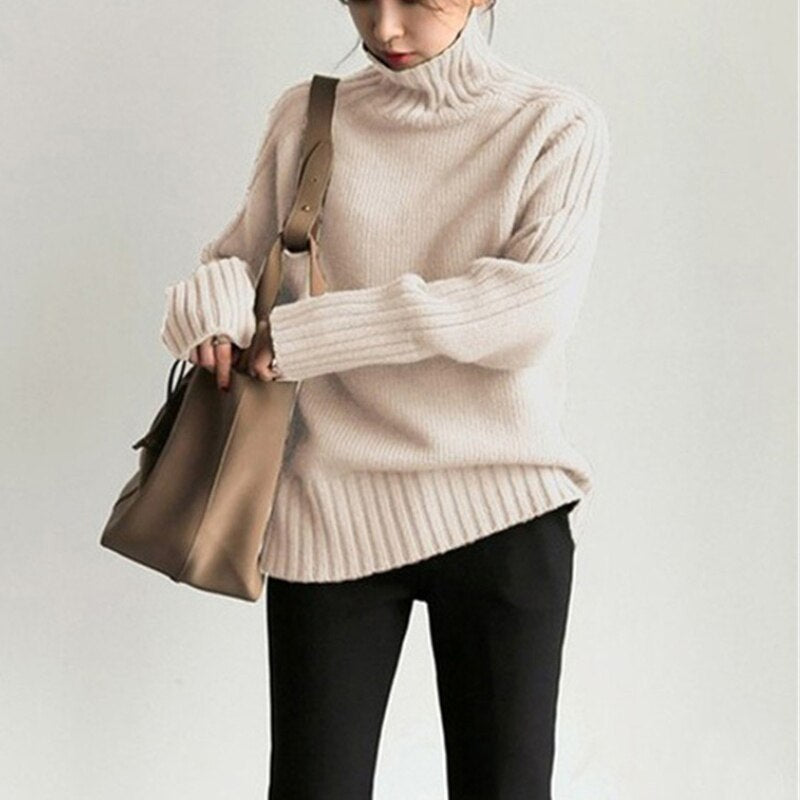 Frau in cremefarbenem Rollkragenpullover und schwarzer Hose, hält eine braune Handtasche. Modetrend, Herbstmode, Damenbekleidung.