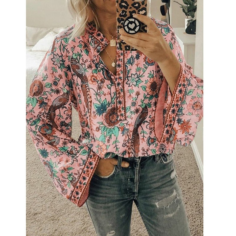 Frau in geblümter Bluse mit weiten Ärmeln, hält Smartphone mit Leopardenmuster-Hülle, trägt Jeans, modisches Outfit, Selfie im Spiegel.