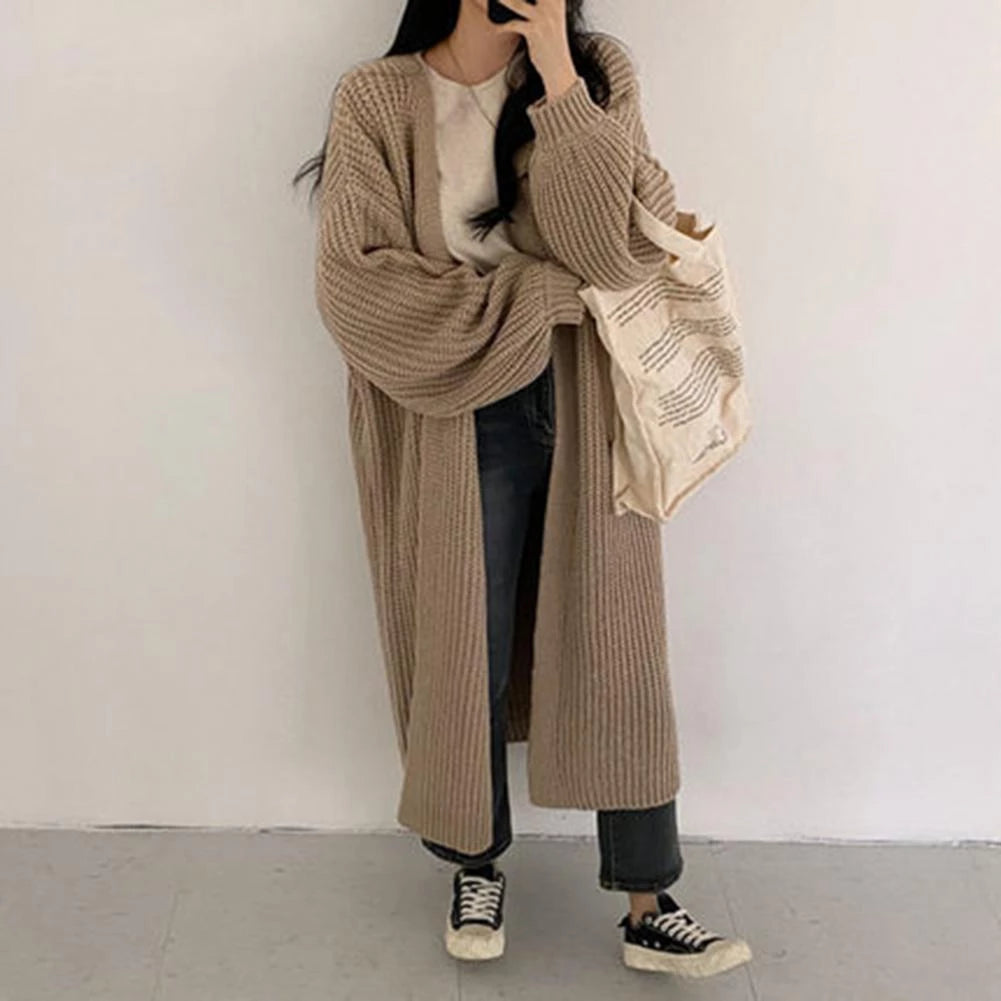 Frau in beigem Strick-Cardigan, weißem T-Shirt und Jeans, hält Stofftasche. Lässiger Herbstlook, Mode, Streetstyle, gemütlich.