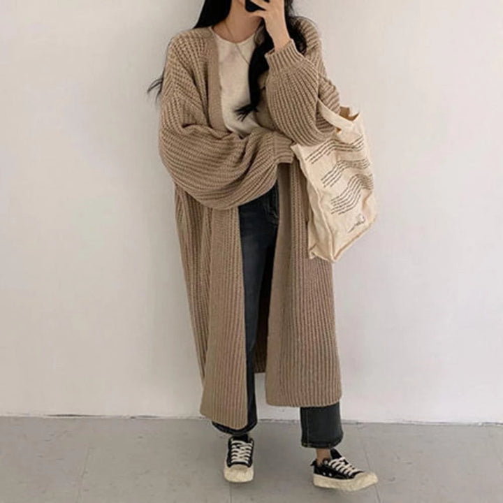 Frau in beigem Strick-Cardigan, weißem T-Shirt und Jeans, hält Stofftasche. Lässiger Herbstlook, Mode, Streetstyle, gemütlich.