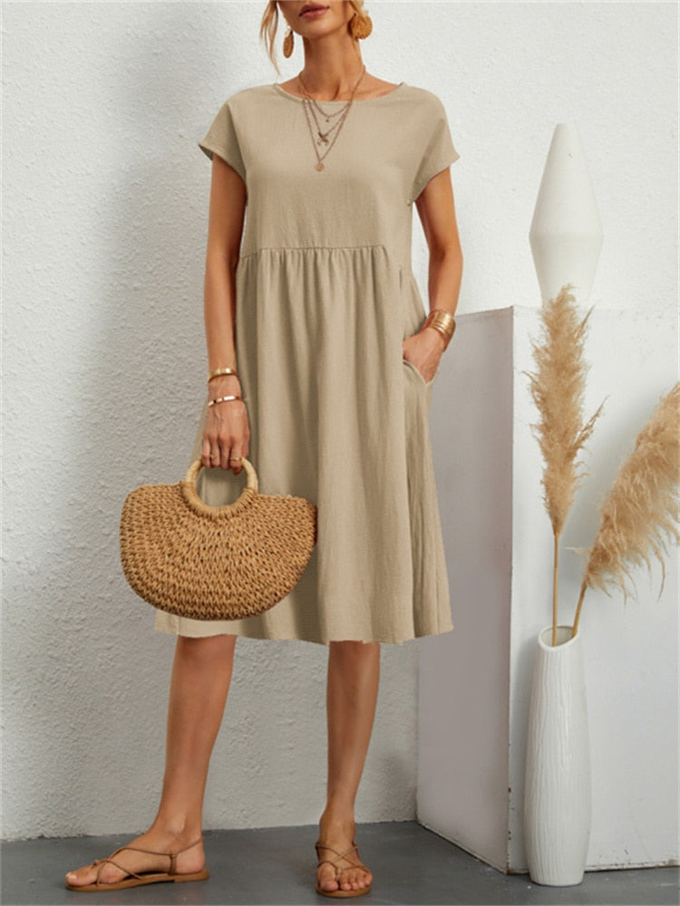 Frau in beige Sommerkleid mit kurzen Ärmeln, hält eine Strohtasche. Steht neben Vase mit Pampasgras. Modetrend, lässiger Stil, Sommermode.