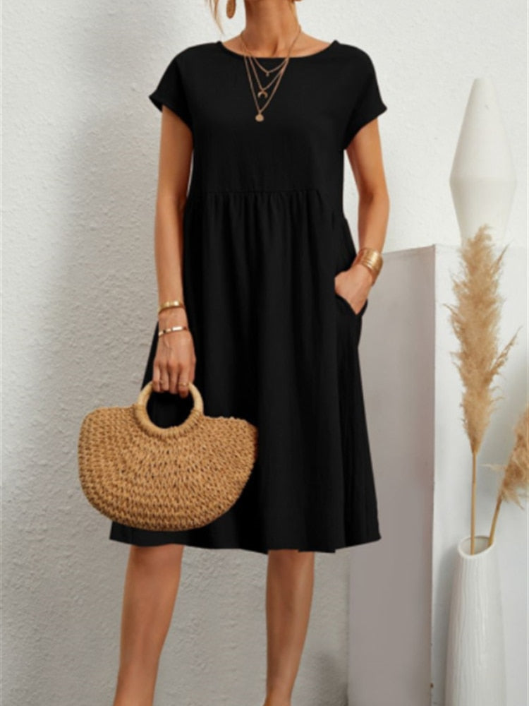 Frau in schwarzem Sommerkleid mit kurzen Ärmeln, hält runde Strohtasche. Minimalistischer Stil, goldene Accessoires, moderne Mode.
